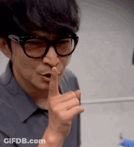A Man Wearing Glasses Is Making A Shhh Gesture GIF