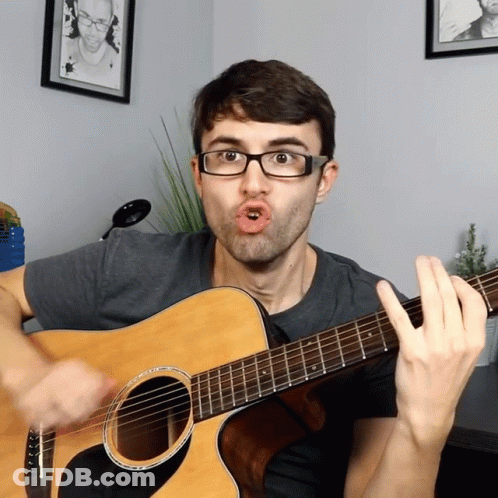 A Man Wearing Glasses Is Playing A Guitar GIF