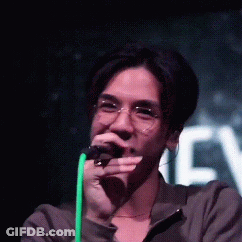 A Man Wearing Glasses Is Singing Into A Microphone On Stage . GIF