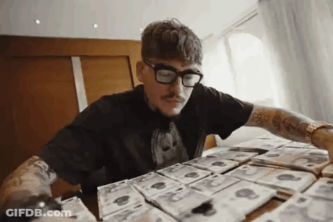 A Man Wearing Glasses Is Sitting At A Table Covered In Money . GIF