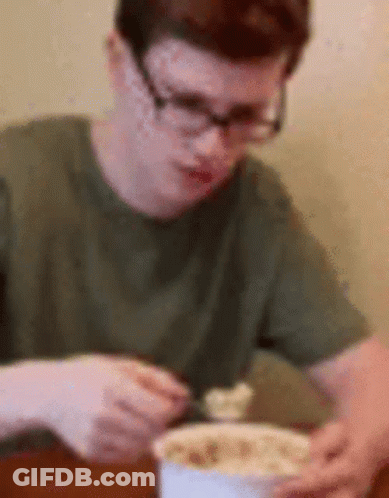A Man Wearing Glasses Is Sitting At A Table Eating A Bowl Of Food GIF