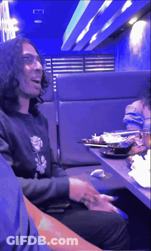 A Man Wearing Glasses Is Sitting At A Table In A Restaurant GIF