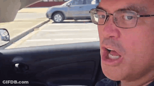 A Man Wearing Glasses Is Sitting In A Car With His Mouth Open GIF