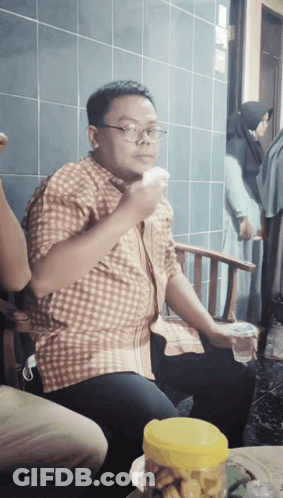 A Man Wearing Glasses Is Sitting In A Chair Eating A Piece Of Food GIF
