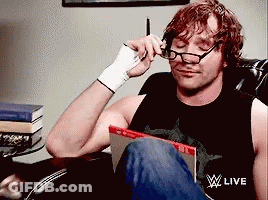 A Man Wearing Glasses Is Sitting In A Chair With A WWE Live Logo On His Shirt GIF