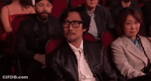 A Man Wearing Glasses Is Sitting In A Theatre Watching A Movie . GIF