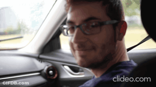 A Man Wearing Glasses Is Sitting In The Driver 'S Seat Of A Car With Clideo.com Displayed On The Bottom GIF