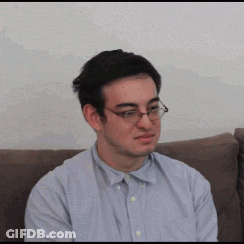 A Man Wearing Glasses Is Sitting On A Couch And Making A Funny Face GIF