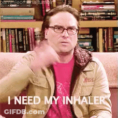 A Man Wearing Glasses Is Sitting On A Couch And Says " I Need My Inhaler " GIF