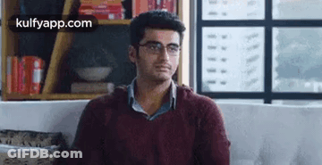 A Man Wearing Glasses Is Sitting On A Couch In A Living Room . GIF