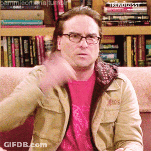 A Man Wearing Glasses Is Sitting On A Couch In Front Of A Bookshelf That Says Trendizisst On It GIF