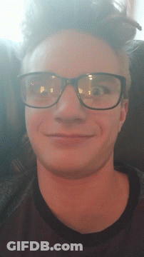 A Man Wearing Glasses Is Smiling And Looking Down GIF