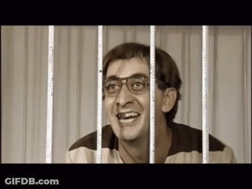 A Man Wearing Glasses Is Smiling Behind Prison Bars GIF