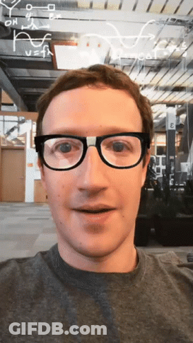 A Man Wearing Glasses Is Smiling In Front Of A Sign That Says " E " On It GIF
