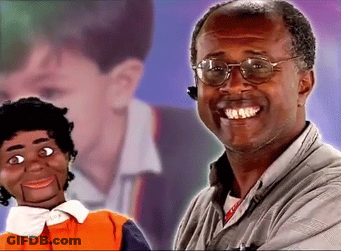 A Man Wearing Glasses Is Smiling While Holding A Puppet . GIF