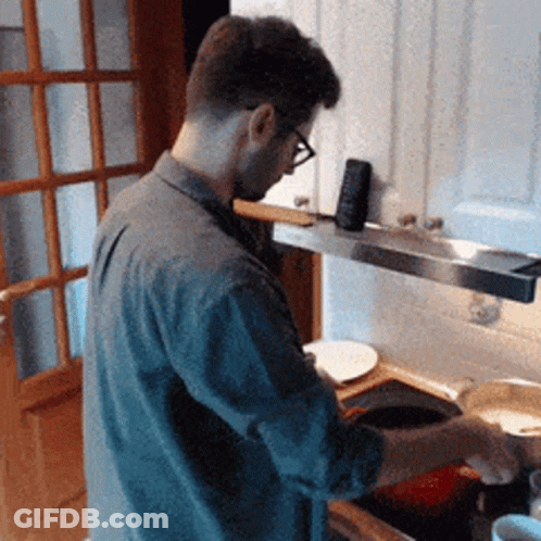 A Man Wearing Glasses Is Standing In A Kitchen Cooking GIF