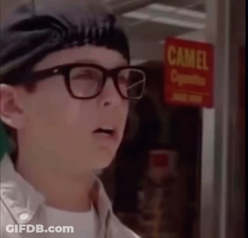 A Man Wearing Glasses Is Standing In Front Of A Camel Cigarette Sign GIF