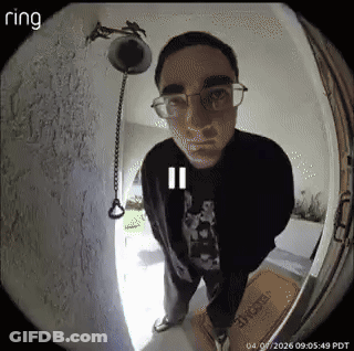 A Man Wearing Glasses Is Standing In Front Of A Door With A Ring Camera . GIF