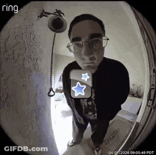 A Man Wearing Glasses Is Standing In Front Of A Door With A Ring Doorbell . GIF