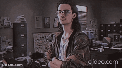 A Man Wearing Glasses Is Standing In Front Of A Sign That Says " Heckerman " GIF