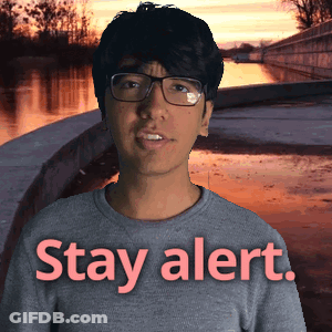 A Man Wearing Glasses Is Standing In Front Of A Sign That Says " Stay Alert " GIF