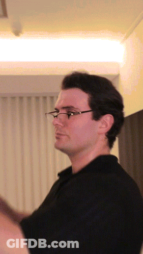 A Man Wearing Glasses Is Standing In Front Of A White Curtain GIF