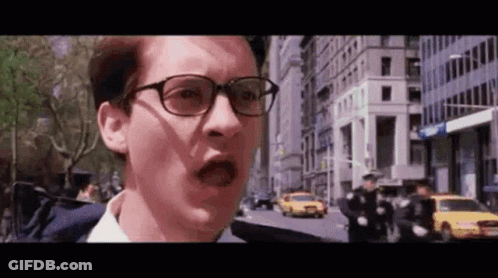 A Man Wearing Glasses Is Standing On A City Street With A Shocked Look On His Face . GIF
