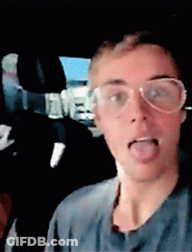 A Man Wearing Glasses Is Sticking His Tongue Out In A Car GIF