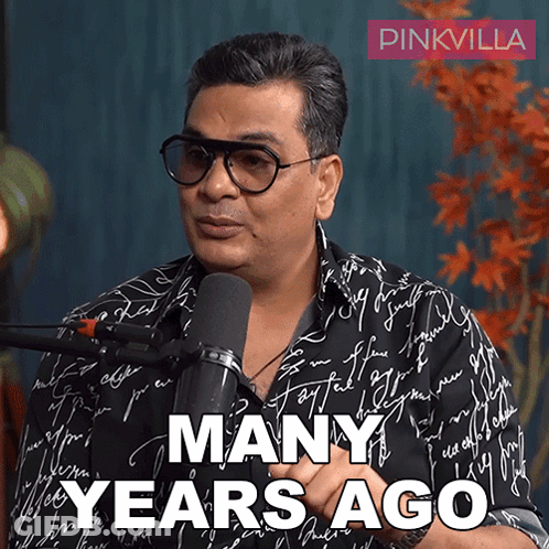 A Man Wearing Glasses Is Talking Into A Microphone With The Words Many Years Ago Below Him GIF