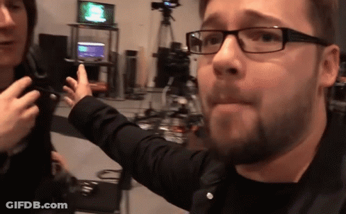 A Man Wearing Glasses Is Talking To Another Man In A Room GIF