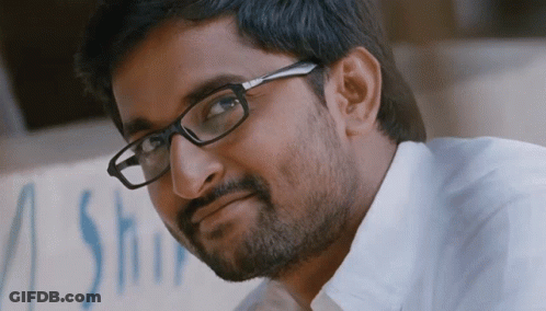 A Man Wearing Glasses Looks At The Camera With A Sign In The Background That Says A Shop GIF