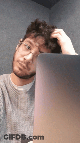 A Man Wearing Glasses Scratches His Head While Looking At A Laptop Screen GIF