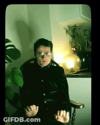 A Man Wearing Glasses Sits In A Chair GIF