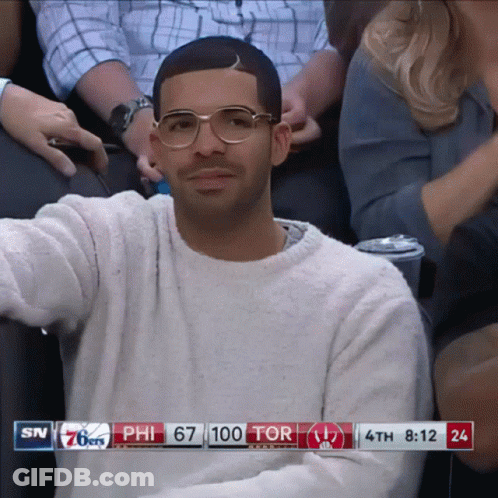 A Man Wearing Glasses Sits In A Stadium Watching A Basketball Game Between The 76Ers And The Tor GIF