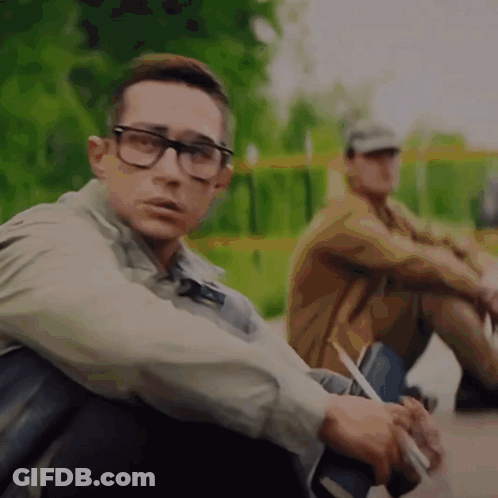 A Man Wearing Glasses Sits Next To Another Man Who Is Smoking A Cigarette GIF