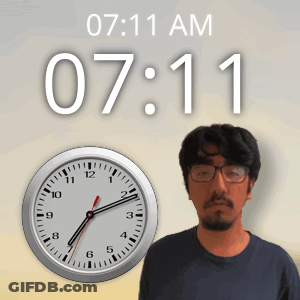 A Man Wearing Glasses Stands In Front Of A Clock That Reads 7:11 Am GIF