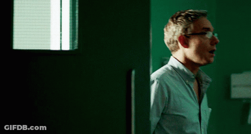 A Man Wearing Glasses Stands In Front Of A Green Wall GIF