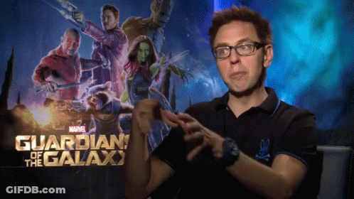 A Man Wearing Glasses Stands In Front Of A Poster For Guardians Of The Galaxy GIF