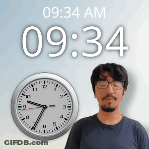 A Man Wearing Glasses Stands In Front Of A Wall Clock That Says 09:34 Am GIF