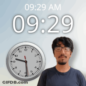 A Man Wearing Glasses Stands In Front Of A Wall Clock That Says 10:29 Am GIF