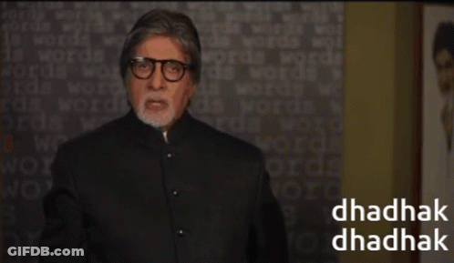 A Man Wearing Glasses Stands In Front Of A Wall With Words On It And The Words Dhadhak Dhadhak On The Bottom GIF