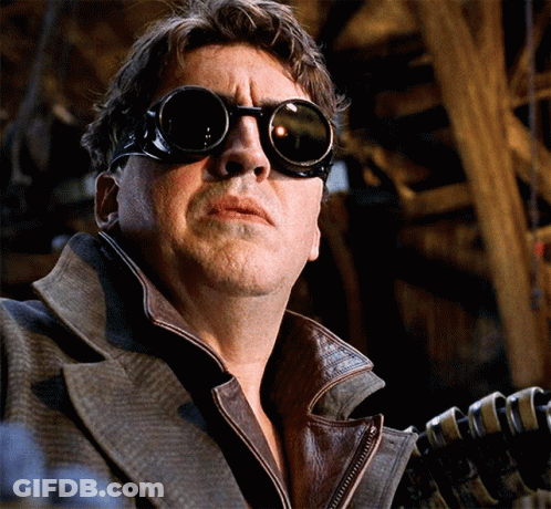 A Man Wearing Goggles And A Leather Jacket Holds A Gun GIF