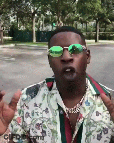 A Man Wearing Green Sunglasses And A Floral Shirt Stands In A Parking Lot GIF