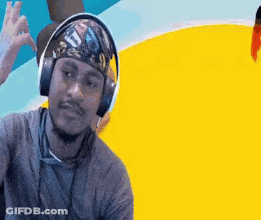 A Man Wearing Headphones And A Bandana Is Giving A Peace Sign . GIF
