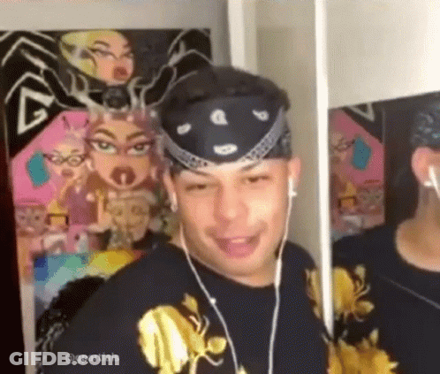 A Man Wearing Headphones And A Bandana Is Looking At Himself In The Mirror . GIF