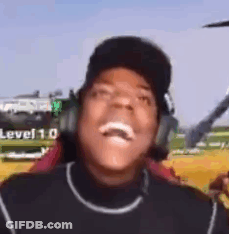 A Man Wearing Headphones And A Baseball Cap Is Laughing In Front Of A Helicopter . GIF