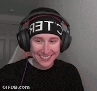 A Man Wearing Headphones And A Beanie Is Smiling And Making A Funny Face . GIF