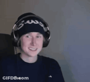 A Man Wearing Headphones And A Beanie Is Smiling While Sitting In Front Of A Computer . GIF
