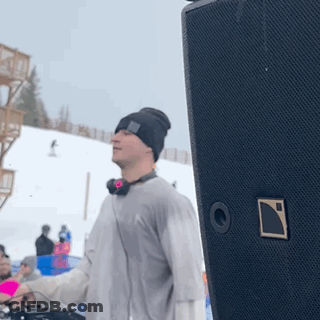 A Man Wearing Headphones And A Beanie Is Standing In Front Of A Speaker GIF