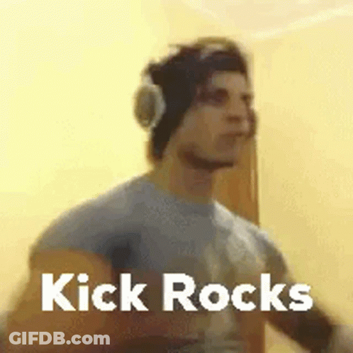 A Man Wearing Headphones And A Beanie Is Standing In Front Of A Wall With The Words Kick Rocks . GIF